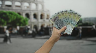 Roma Kolezyumu 'nun yakınında elinde Romen banknotları tutan erkek el, antik bir şehir sokak ortamının kalbinde kültür, seyahat ve finans kaynağını yakalıyor..