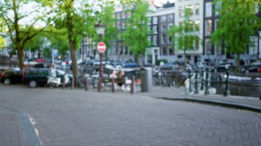 Amsterdam 'da bulanık bir manzara. Kanal, ağaçlar, bisikletler ve kentin manzarasını ve sakin atmosferini gösteren binalar..