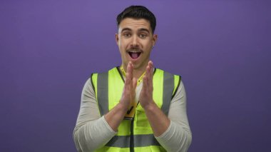 Yansıtıcı yelek giyen genç adam, izole edilmiş mor duvara karşı kamu hizmeti projesinde gönüllü olarak duruyor.