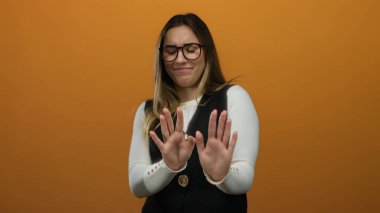 Gözlüklü bir kadın, portakal rengi bir arka plana karşı reddedilme hareketi gösteriyor. Ayrı bir ortamda, kaldırılmış bir elden ve hoşnutsuzluktan hoşnutsuzluğunu dile getiriyor..