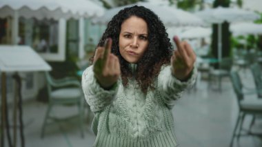 İspanyol kadın restoranın terasında el kol hareketleri yapıyor. Açık havada hayal kırıklığını dile getiriyor. Orta parmakları havada, duygusal bir anı yakalıyor..