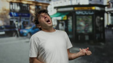 İspanyol bir adam komik bir ifade takınıyor ve kalabalık bir sokakta gitar çalıyor gibi yapıyor. Canlı etkinliklerle dolu bir şehir ortamında mizah ve yaratıcılık ifade ediyor..