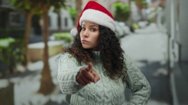 Noel Baba şapkalı bir kadın sokakta ciddi bir ifadeyle işaret ederken hayır işareti yapıyor. Tatil temalı açık hava projeleri için uygun neşeli ama sıkı bir ruh hali yakalıyor..