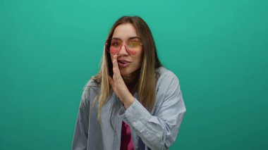 Canlı, yeşil bir arka plan, neşeli pembe güneş gözlüklü bir kadın gizlice fısıldıyor. Canlı ve genç bir hava veriyor..