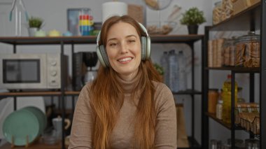 Konforlu ofis mutfağında kulaklıklarla gülümseyen bir kadın raflar, mikrodalga fırınlar ve bulaşıklar, keyif ve rahatlığa odaklı rahat bir çalışma ortamı öneriyor..