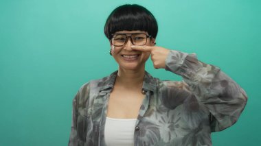 Gözlüklü genç Çinli kadın, yeşil bir arka plana bakarak mizah ve kendine güveni ifade ediyor..