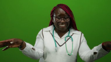 Gözlüklü ve steteskoplu kadın yeşil arka planda el hareketleriyle gülümsüyor, beyaz giyiniyor, enerji ve iletişim taşıyor, izole ortama karşı.