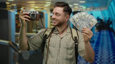 Spor salonunda gülümseyen ve fotoğrafçılıktan zevk alan kameralı genç bir adam Amerikan parası ve seyahat macerası sergiliyor..