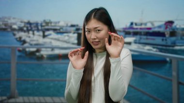 Arka planda teknelerle deniz kenarında duran bir kadın, çevreden rahatsız görünüyor, düşünce sahnesini yansıtıyor ve dışarıda huzursuzluk yaratıyor..