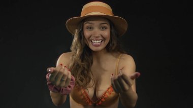 Stüdyoda, turuncu bikinili ve hasır şapkalı genç İspanyol kadın parmaklarını işaret ediyor..