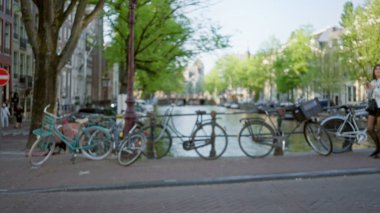 Bulanık görüntü, güneşli bir günde arka planda çözünmüş bir kadınla bir ambu kanalı boyunca dizilmiş bisikletlerin sakin bir Hollanda kentsel atmosferi yarattığını gösteriyor..