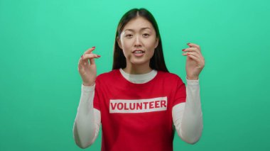 Kadın gönüllü kırmızı gömlek giyerken canlı yeşil arka plana karşı coşkuyla el kol hareketi yapıyor.