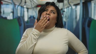 Otobüste esneyen bir kadın, kentsel toplu taşıma ortamında yorgunluğunu ifade eden, gerçek hayatta işe gidip gelme sahnesinde çeşitliliği ve duyguyu ön plana çıkaran bir kadın..