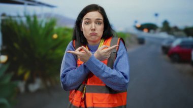 Sokakta duran turuncu yelek giyen kadın şüpheli bir şekilde esmer gönüllüyü işaret ediyor. Bulanık şehir arka planına kafa karıştırıcı bir şekilde işaret ediyor..