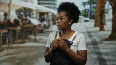 Önlüklü kadın hareketli bir açık hava restoranının terasında duruyor. Canlı bir şehir yemeği ve sokak hayatı sahnesi sergiliyor..