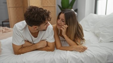 Kadın ve erkek rahat bir yatak odasında birlikte uzanıp pencerelerden süzülen doğal ışıkla huzurlu bir evde sevgi ve yakınlık ifade ediyorlar..