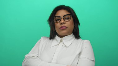 Gözlüklerini yeşil arka plana göre ayarlayan, beyaz gömlek giyen, büyük beden giyen, yalıtılmış ortamda Latin güzelliğini gösteren, modern tarz ve güç veren bir kadın..