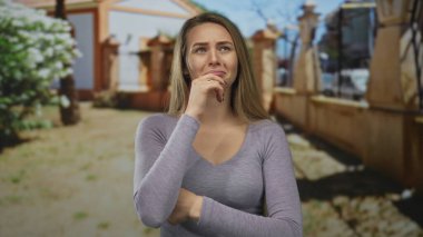 Parkta yüzü koyun ağlayan kadın, doğal ortamda ayakta duran, güneşli koşullar altında günlük giysiler giyen, doğada duygusal sıkıntı ya da neşe olduğunu öne süren kadın..