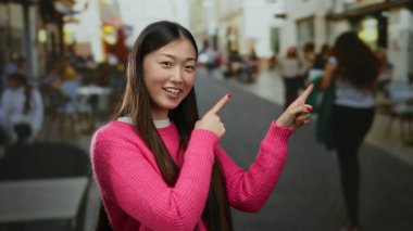 Parlak pembe süveter giyen kadın, şehir sokaklarında arka planı bulanık, modern gençlik enerjisi ve açık hava nişanı somutlaştıran ilginç bir şeye işaret ediyor..