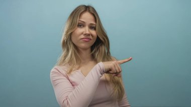 Ciddi ifadeleri olan sarışın kadın mavi stüdyoyu işaret ediyor; suçlama onaylanmamış eleştiri.