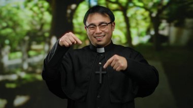 Papazlar gibi giyinmiş Asyalı bir adam arka planda yemyeşil ağaçlarla dolu bir parkta gülümsüyor. Dini bağlılığını ve huzur dolu sükunetini sergiliyor..