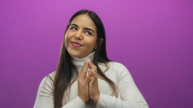 Portre, elleri sımsıkı bağlanmış bir kadını izole edilmiş, genç Latin kökenli pembe arka plan duvarının önünde komplo kurarken gösteriyor..