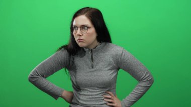 Gözlüklü kadın, parlak yeşil bir arka plana karşı ifadeler sergiliyor gri bir kazak giyiyor duyguları ve doğal güzelliği yakalıyor.
