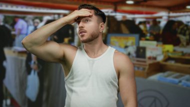 Beyaz gömlekli genç adam, renkli tezgahlar ve bulanık alışveriş geçmişiyle hareketli bir açık hava market sahnesinde derin derin poz veriyor..