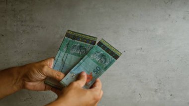 Malezya ringgit notları tutan adam somut bir arka plana karşı, Malezya 'daki finansal kavramları ve para birimini vurguluyor.