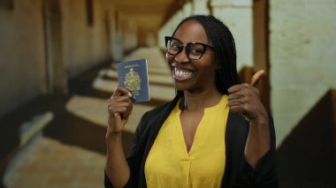 Kanada pasaportlu akademik bir ortamda gülümseyen bir kadın, sarı giyinmiş, başarıyı somutlaştıran ve çok kültürlülüğü somutlaştıran, bir üniversite koridorunda güvenle duran.