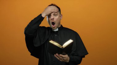 Genç rahip parlak turuncu arka planda sürpriz bir şekilde İncil okuyor, dini bağlılık ve beklenmedik keşifler sergiliyor..