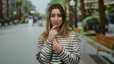 Bulanık bir sokakta duyguları ifade eden genç sarışın bir kadın. Banklar ve ağaçlarla sakin bir zemin oluşturuyor..