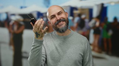 Araba anahtarlarını tutan sakallı adam arka planda insanların bulanıklaştığı bir sokakta gülümsüyor, hareketli bir şehir ortamında neşeli bir an sergiliyor..