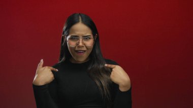 Kadın, arka plan duvarının önünde izole edilmiş genç bir Latin Latin mankeni canlandırarak, kırmızı ekranda el kol hareketi yaparak parmağını tıklatıyor..