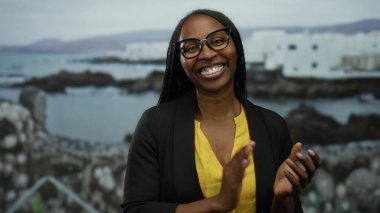 Sahilde deniz kenarında dalgalı saçlarıyla gülümseyen kadın manzaralı deniz manzaralı ve arka planda binaları olan.