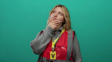 Yeşil arka planda gönüllü olan kırmızı yelekli bir kadın.