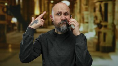 Müzede sakallı, telefonda konuşan kel bir adam evde el hareketleriyle hayal kırıklığını gösteriyor. Stres iletişimi kurarken kafkasyalı erkek dövmesi yaptırıyor..