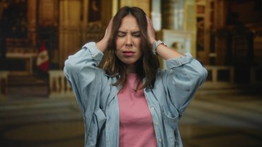 Kilise ortamında stresli hisseden bir kadın, büyük mimariyle çevrili, duygusal bir anı Peru bayrağıyla yakalıyor, İspanyol kökenini ve kapalı ortamını vurguluyor..