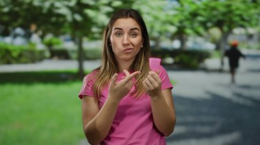 Parkta elinde regl fincanı tutan bir kadın, pembe tişörtlü, düşünceli bir yüz ifadesi olan, yeşil bulanık arka planda duran, çevre dostu yaşam tarzı tercihlerini vurgulayan..