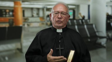 Koyu renk cüppeli başrahip bir havaalanında bir kitap tutuyor. Bulanık oturma alanı olan modern bir ev ortamını işgal ediyor. Seyahat ya da ruhsal seyahat anlamında..