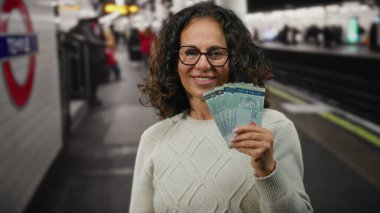 Tren istasyonunda gülümseyen bir kadın elinde Malezya bankası banknotları ile, bir şehir taşımacılığı ortamında zenginlik ve kültürel çeşitlilik sergiliyor..
