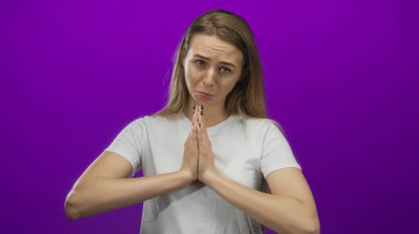 Dua eden elleri olan genç bir kadın, canlı mor bir zemin üzerinde poz veriyor. Stüdyo ortamında umut ve tefekkür taşıyor..