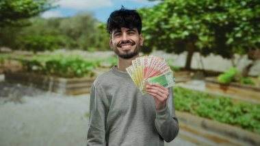 Parlak bir park ortamında Norveçli banknotları elinde tutan adam yemyeşil, parlak doğal bir ortamda gösteriş yapan paralarla güvenle gülüyor..