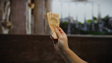 Bir şehir caddesinde el ele tutuşan Brezilyalı gerçek banknotlar, para ve ekonomi odaklı kentsel bir ortamda iş ve finans özünü yakalıyor..