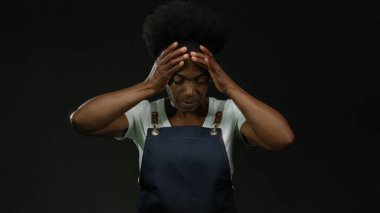 Önlüklü kadın, iş yerindeki stresi vurgulayan siyah arka plana karşı hayal kırıklığı içinde..