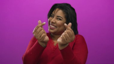 Kırmızı kazaklı bir kadın pembe arka planda kalp işareti yapıyor izole bir ortamda mutluluk ve pozitiflik gösteriyor.