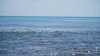 Akdeniz dalgaları güneşli açık deniz sahillerine huzur verici bir ufuk ile çarpar, dingin bir arka plan veya tatil teması için idealdir..