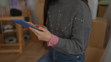 Karton kutularla dolu yeni bir dairede rahat bir süveter giyen kadın, yeni bir eve taşınmanın ve rahat bir yaşam alanı kurmanın heyecanını sergiliyor..