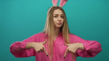 Pembe gömlekli ve paskalya tavşanı kulaklı bir kadın canlı yeşil bir arka plana doğru hareket ediyor. Yaratıcı ya da şenlikli kavramlar için izole edilmiş..