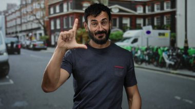 Sokak ortasında İspanyol bir adam şehir binalarının önünde el kol hareketleri yapıyor ve park halindeki araçlar samimi bir ifade ve duygu anı yakalıyor..